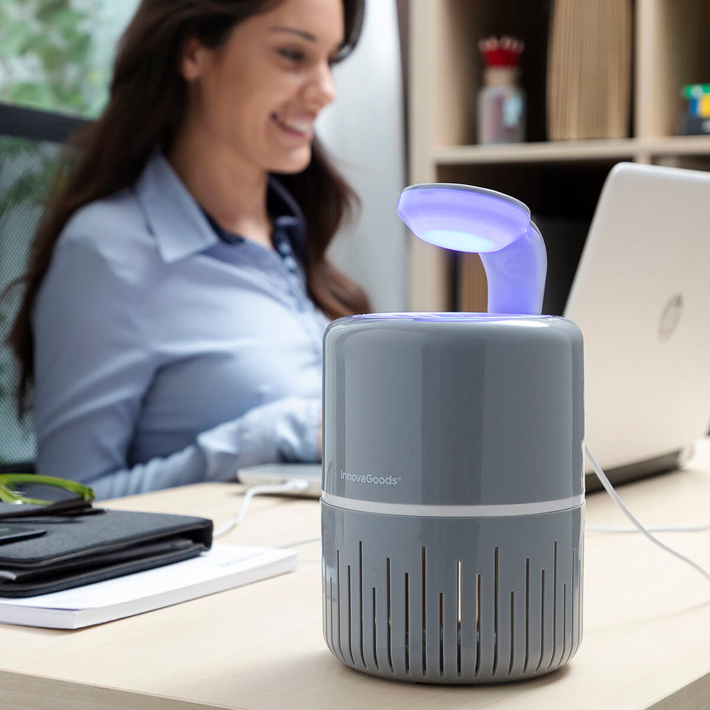 A lifestyle image showing the mosquito lamp on a desk while a woman works on her laptop. The lamp is lit, creating a calm and focused work environment.