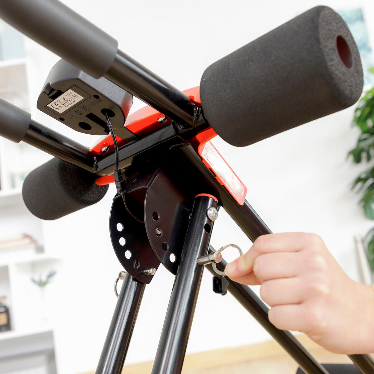 A hand adjusting the pin on the Folding Abdominal Machine, highlighting its adjustability and ease of use. The black and red color scheme is prominent.