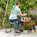 A woman seated on a green and gray folding garden stool, with a gray tool bag attached, in a garden setting. She is tending to potted plants on a wooden table nearby.