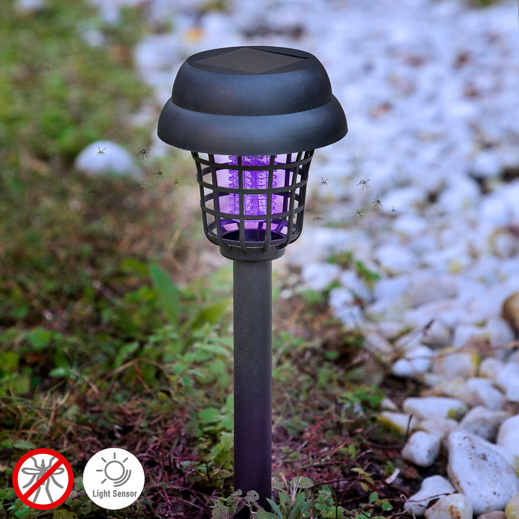 The lamp is shown installed in a garden setting, with a glowing purple light attracting mosquitoes. The background consists of greenery and stones. There are icons indicating 'no mosquitoes' and 'light sensor'.