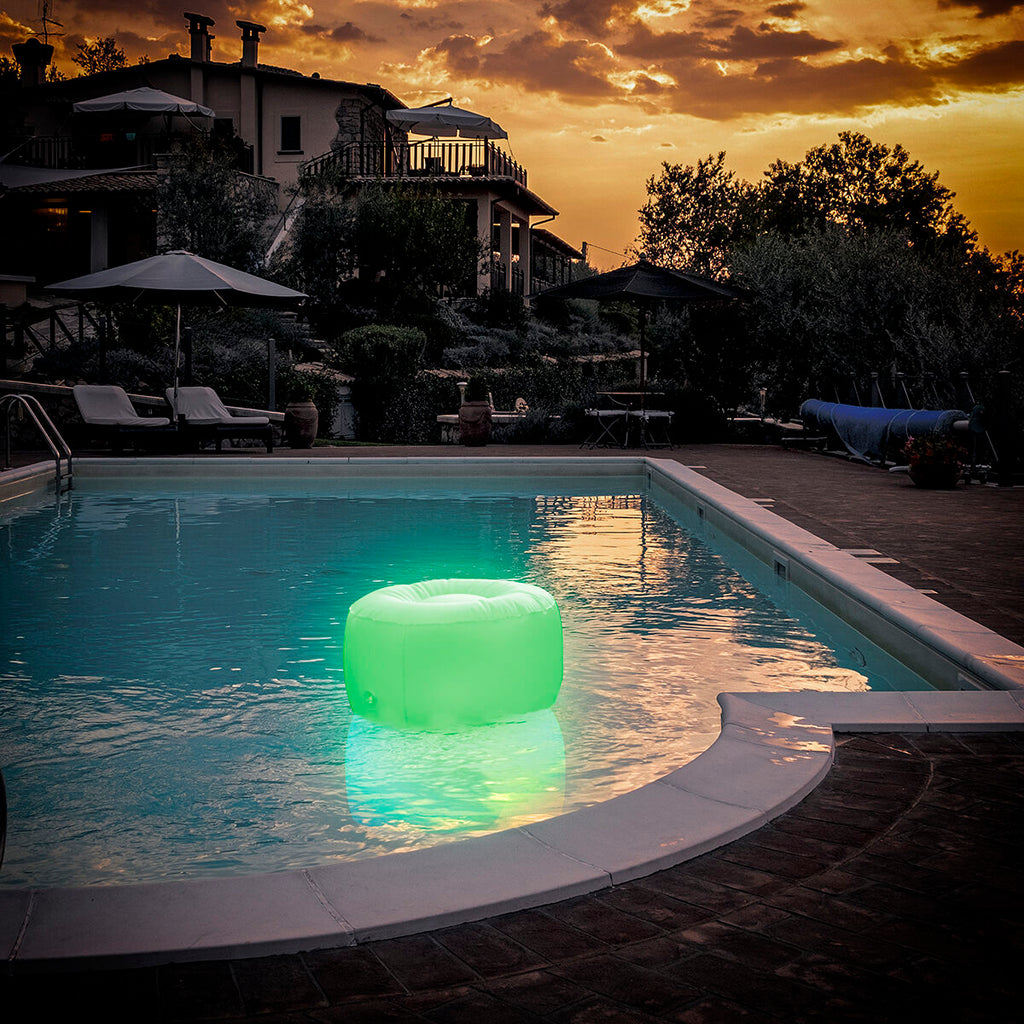 The inflatable LED seat floating in a swimming pool during sunset, lit up with a green color, adding ambiance to the setting.