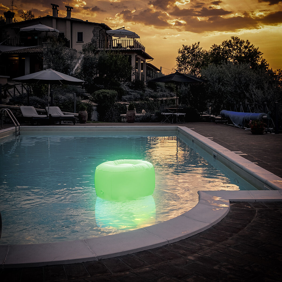 The inflatable LED seat floating in a swimming pool during sunset, lit up with a green color, adding ambiance to the setting.