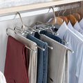 Hanger in use in a closet, holding various colored trousers with additional shirts on wooden hangers in the background.