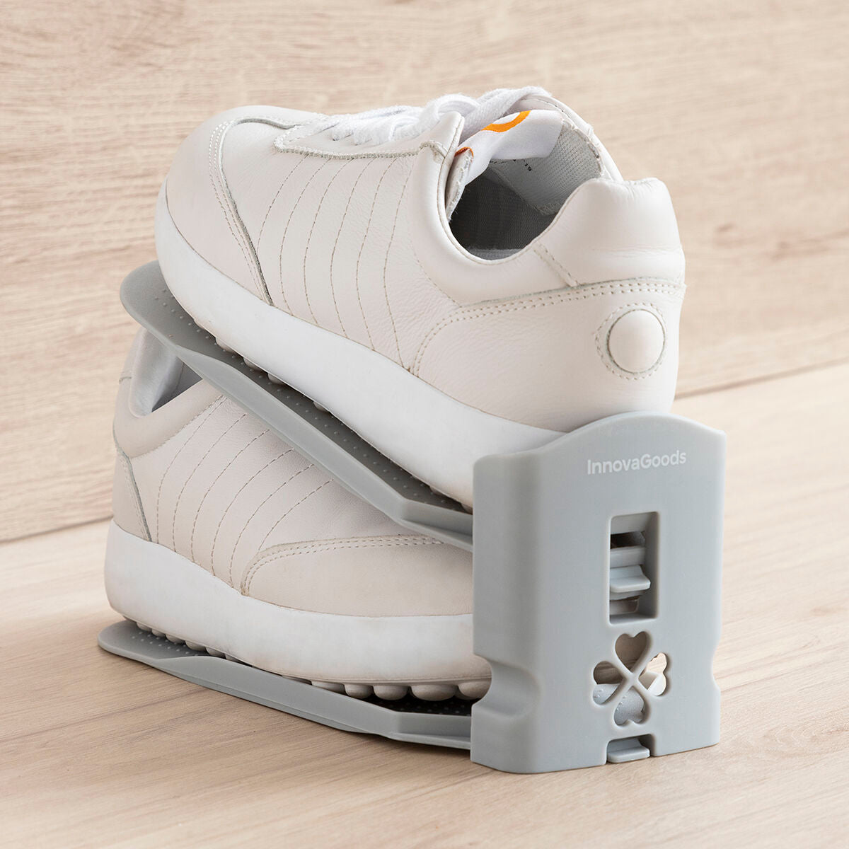A casual setting image with a pair of white sneakers fitting snugly in the shoe organizer. The organizer's gray color contrasts neatly with the wooden backdrop.