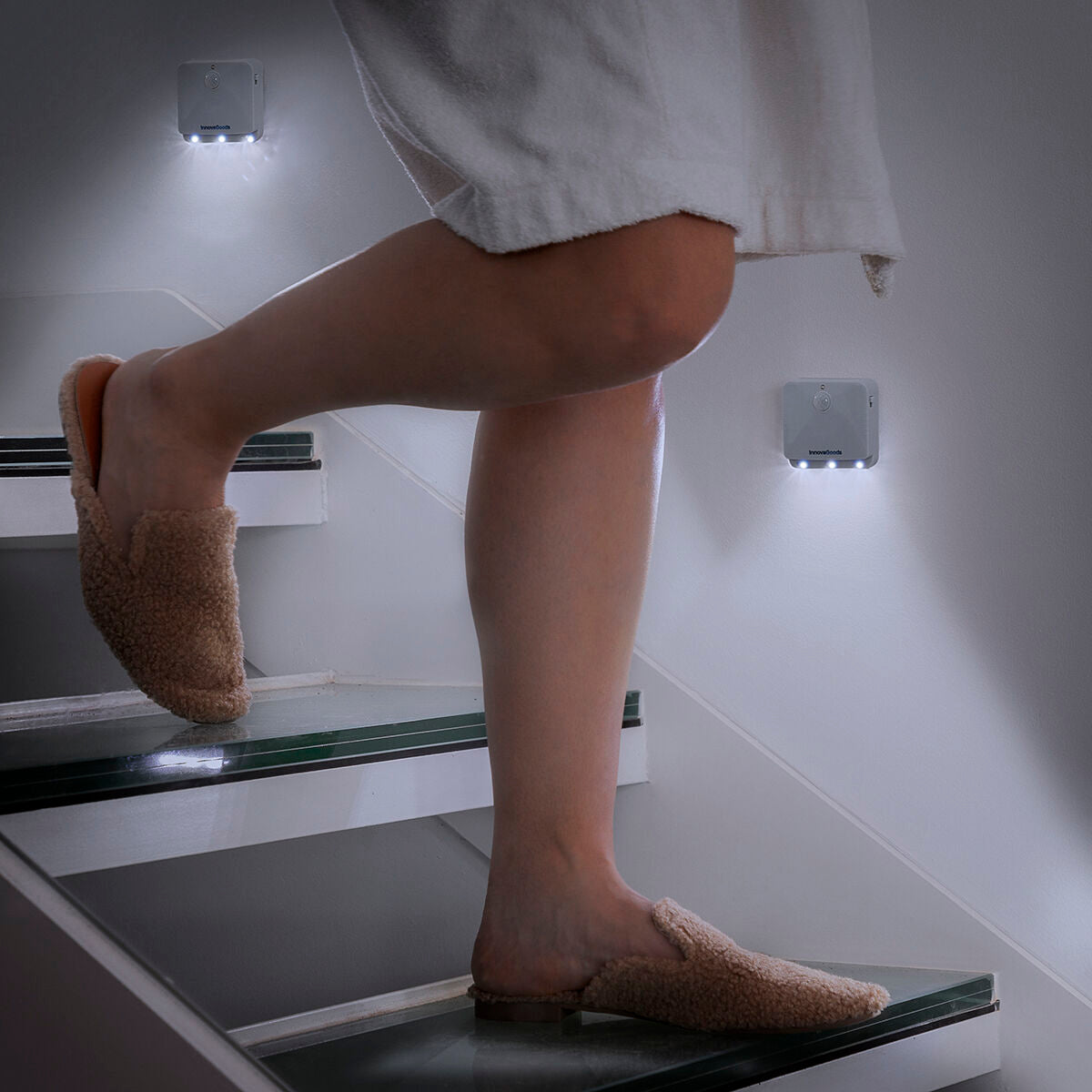A lifestyle image showing a person's legs as they walk down a staircase at night, with the LED motion sensor lights installed on the wall illuminating the steps.