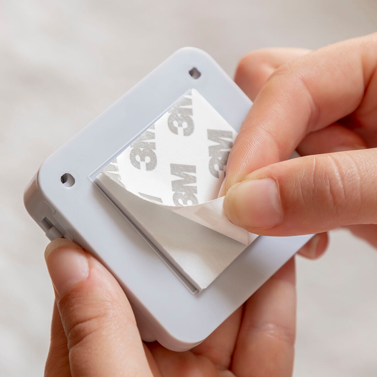 A person's hands peeling off 3M adhesive backing, illustrating ease of installation.
