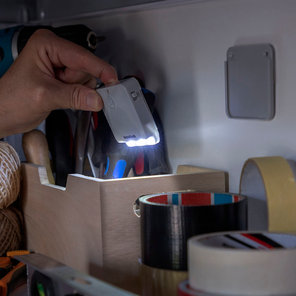 A hand is seen using the LED light as a torch in a tool closet, mounted on the wall.