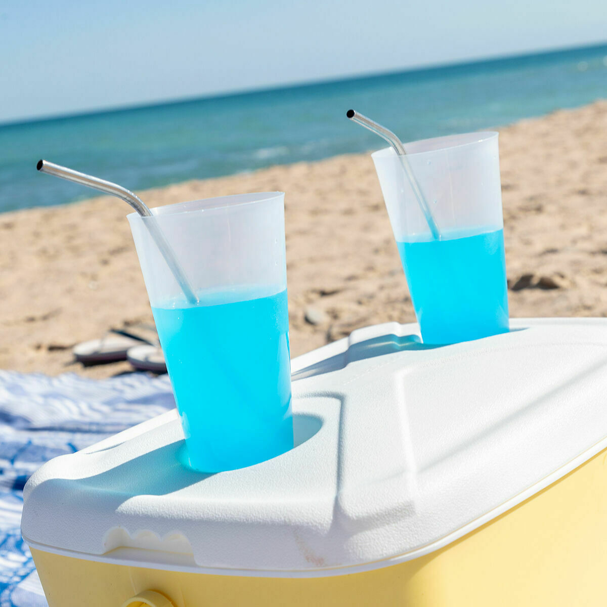 Close-up of drinks placed on the cooler's lid at the beach, showing cup holder feature.