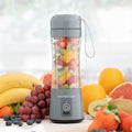 The blender is displayed filled with chopped fruits like strawberries, kiwi, and orange, emphasizing its use for fresh smoothies. It has a gray base, with the InnovaGoods logo and a power button. The background includes various whole fruits, creating a vibrant, healthy setting.