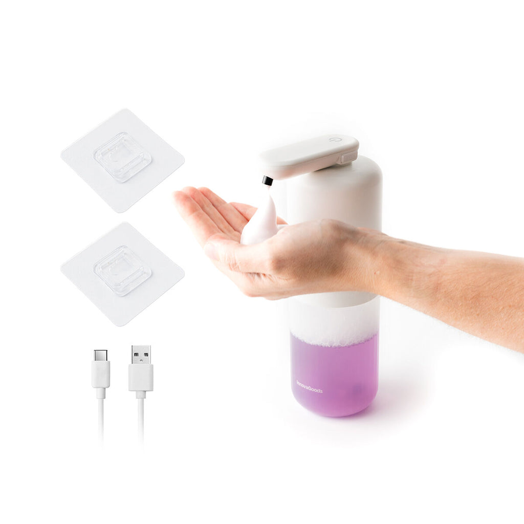 The soap dispenser is shown in use with a hand receiving foam. Two adhesive pads and a USB charging cable are shown next to it.