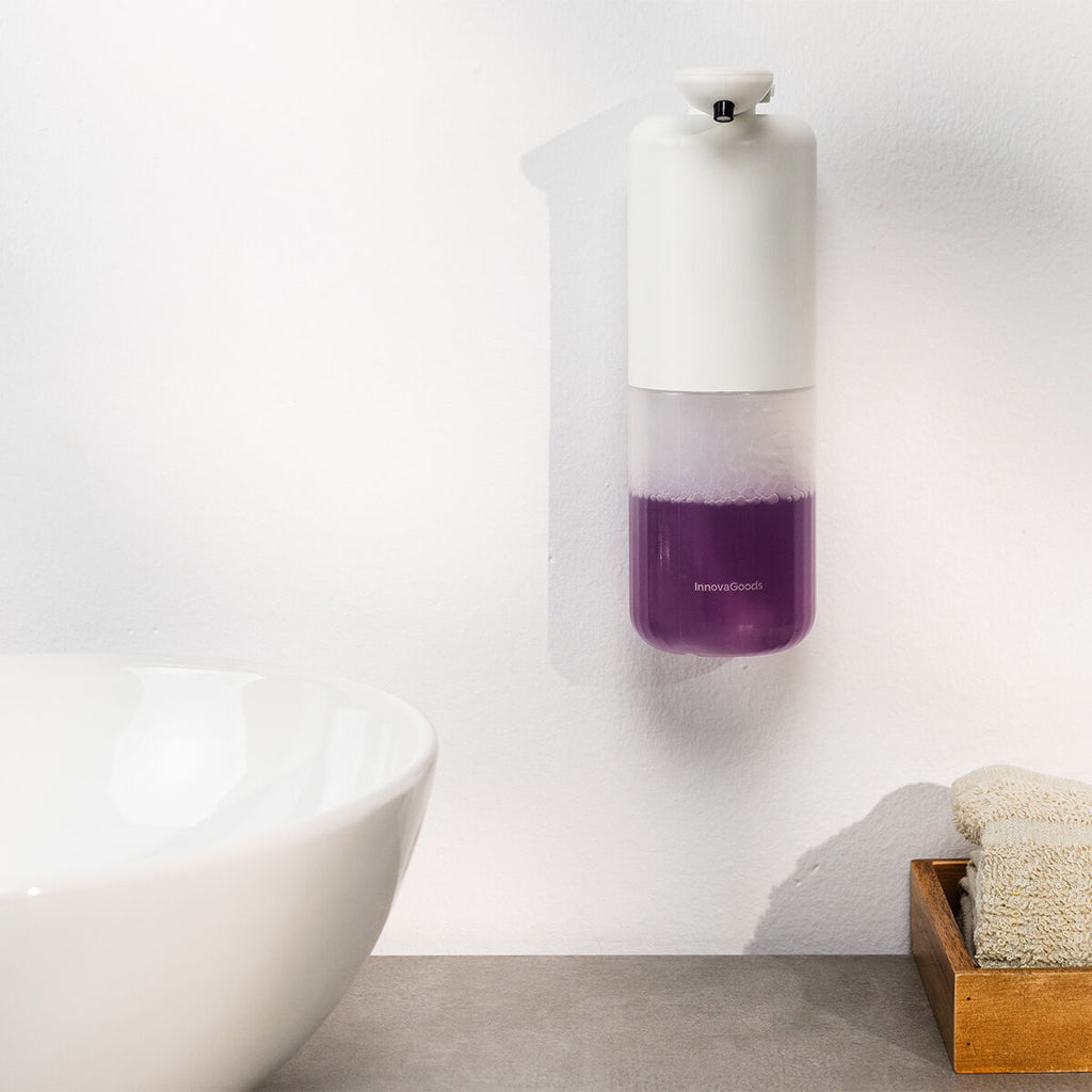 The soap dispenser is mounted on a wall above a bathroom sink, showing the clear bottom filled with purple soap.
