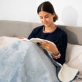 A person sitting on a bed with a grey electric blanket, engaged in reading.