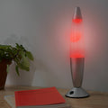 The lamp is illuminated with a red light, placed on a wooden desk near a plant and a book, demonstrating its ambient lighting capabilities.