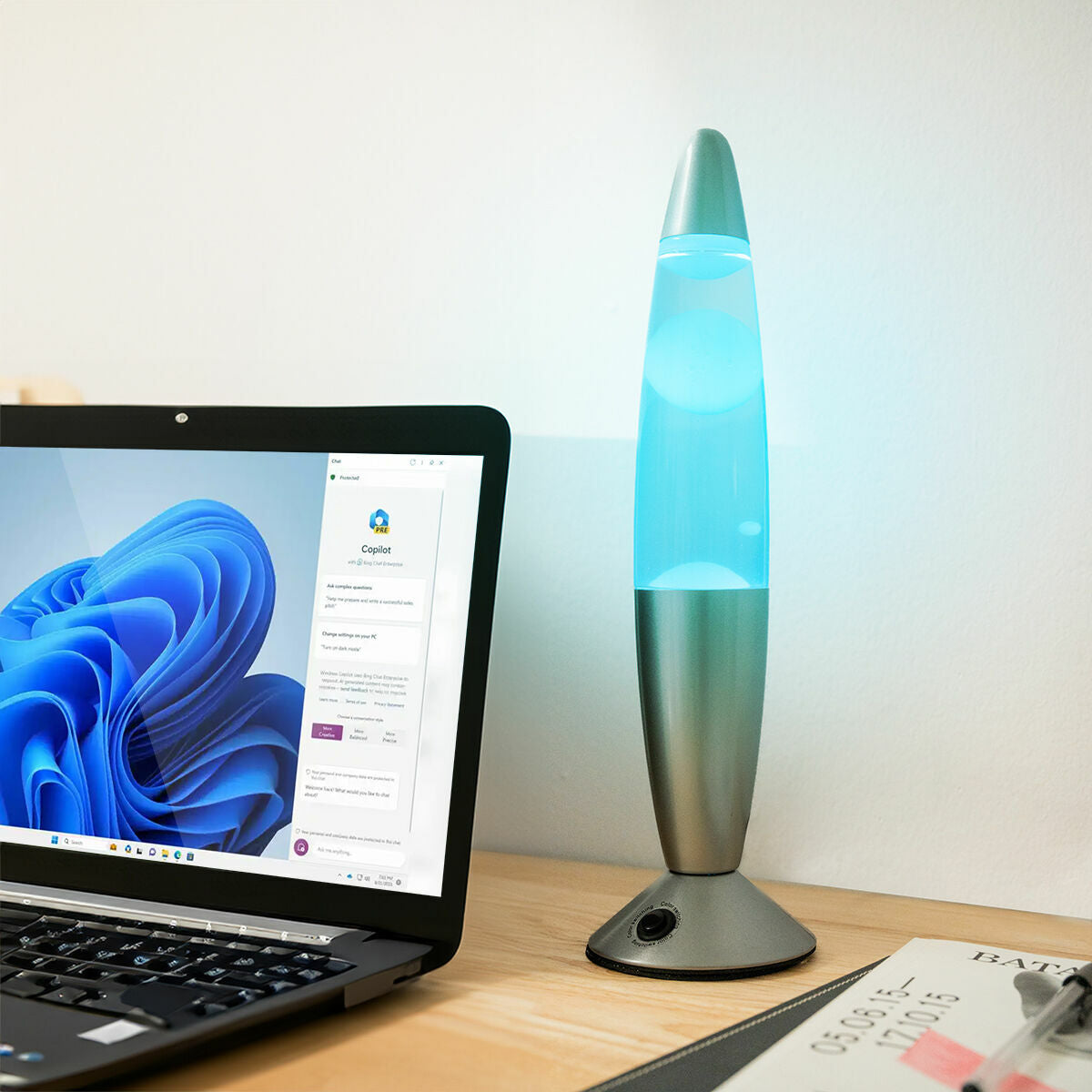 The lamp lit with a blue LED light on a desk next to a laptop, illustrating its use in a home office setting.