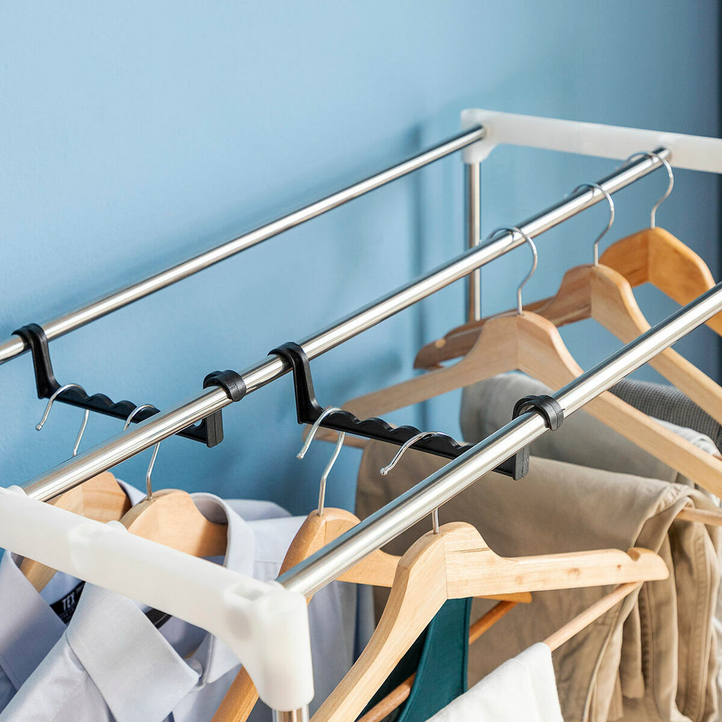 Close-up of the top rods of the dryer with several clothes hangers attached, indicating capacity and organizational features. The background is a light blue wall with casual clothing draped on hangers.