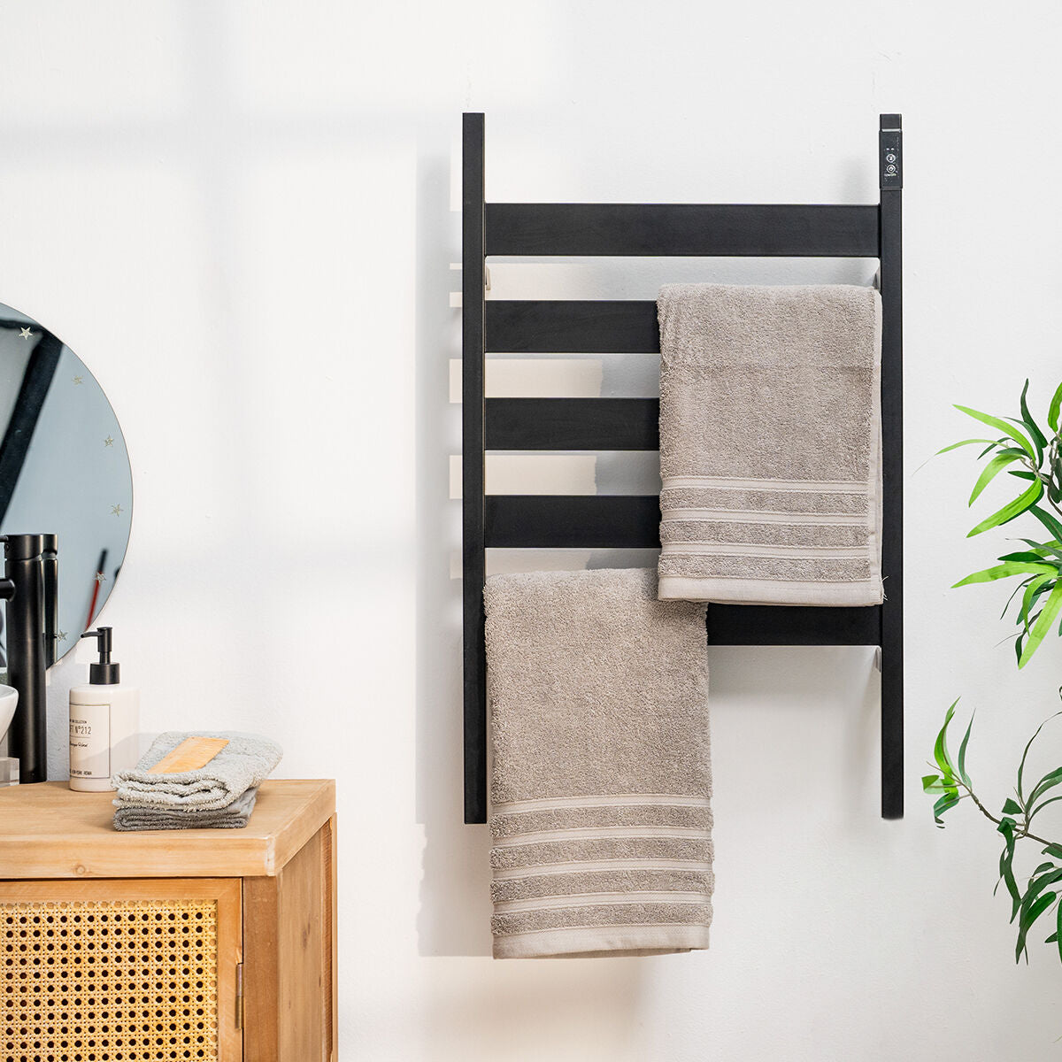The product in a bathroom setting, mounted on the wall with towels hanging, against a white wall with natural wood furnishings.