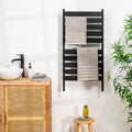 The towel rail is wall-mounted in a bathroom setting, alongside wooden and wicker furniture, with folded towels hanging. The aesthetic is clean and natural, with a plant adding a touch of greenery.