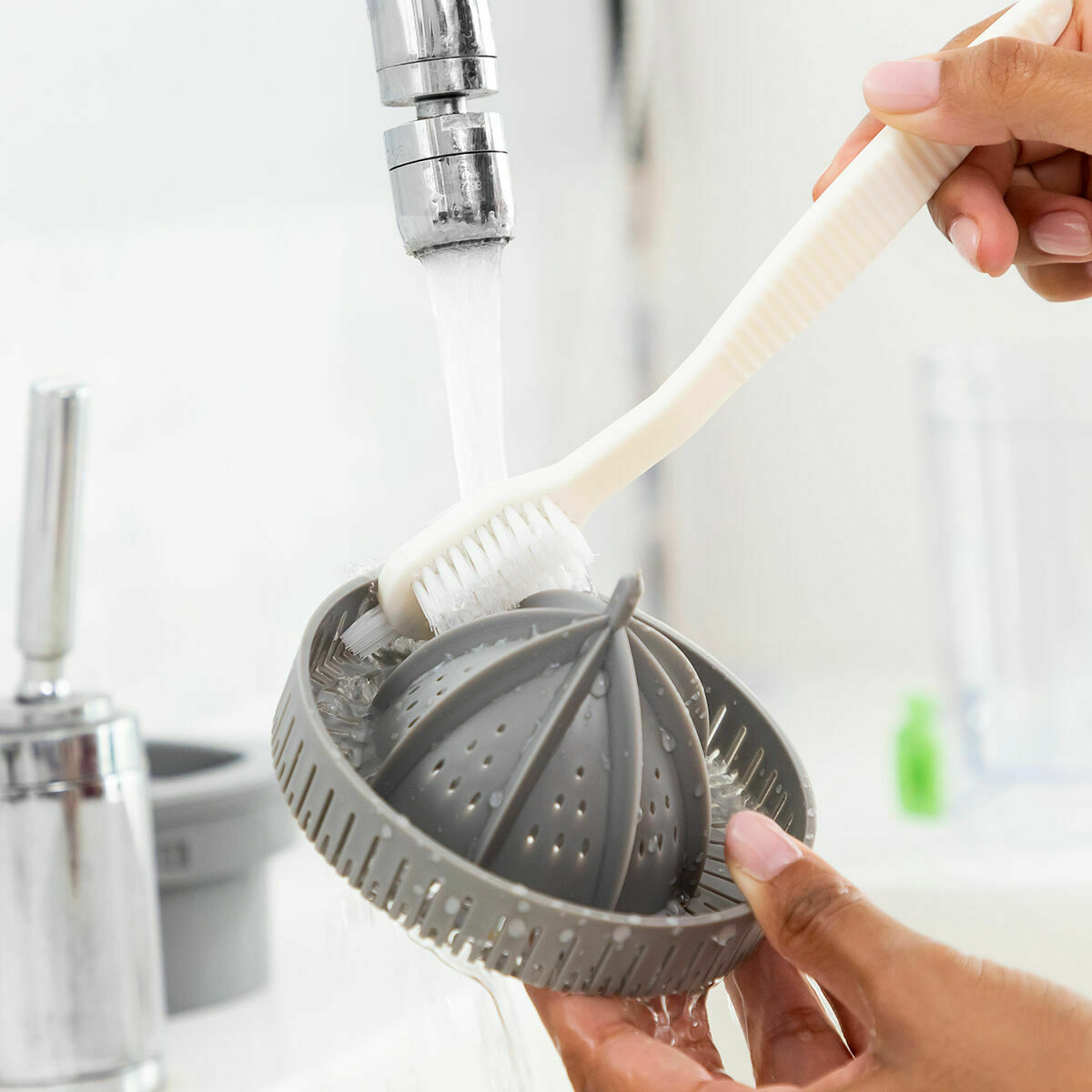 Juicer part being cleaned under running water with a brush.