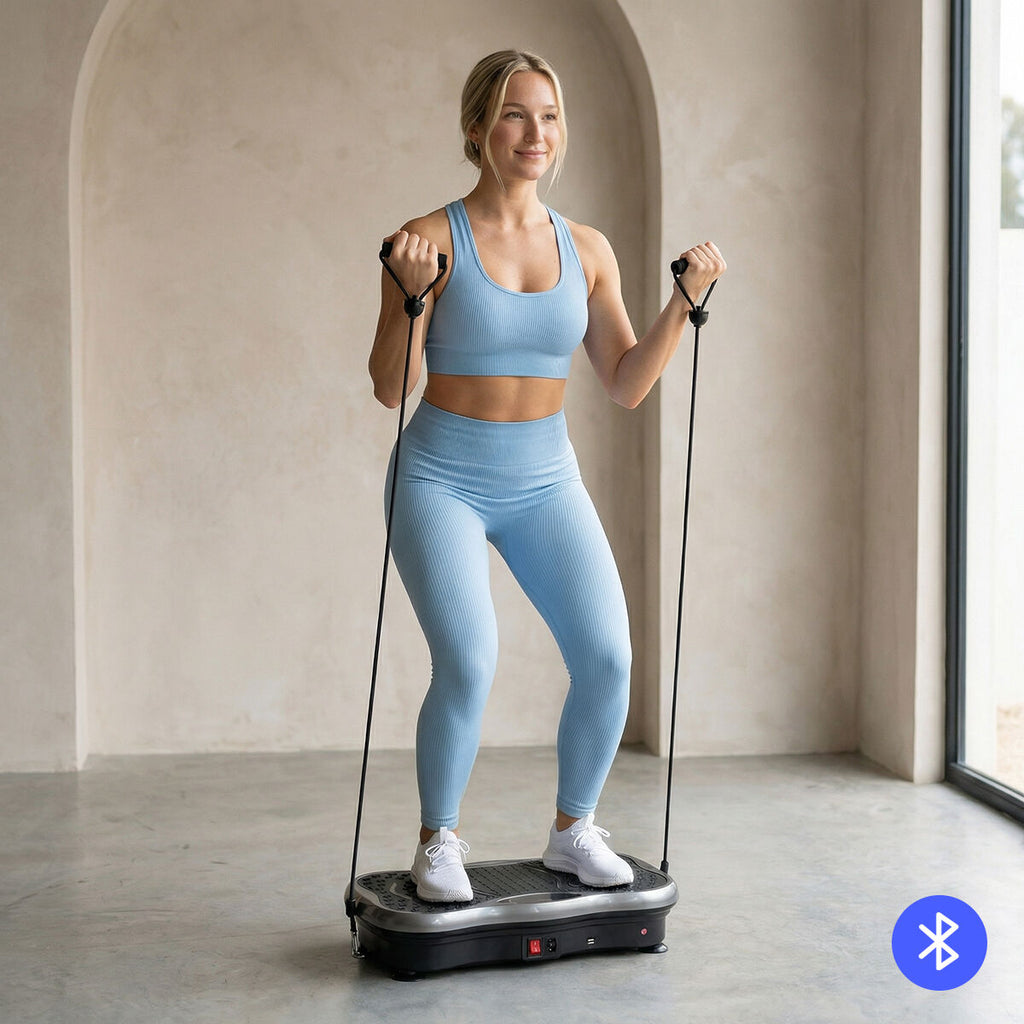A woman in light blue workout attire stands on the vibration platform, using resistance bands. The background is a minimalist room with an arched wall.