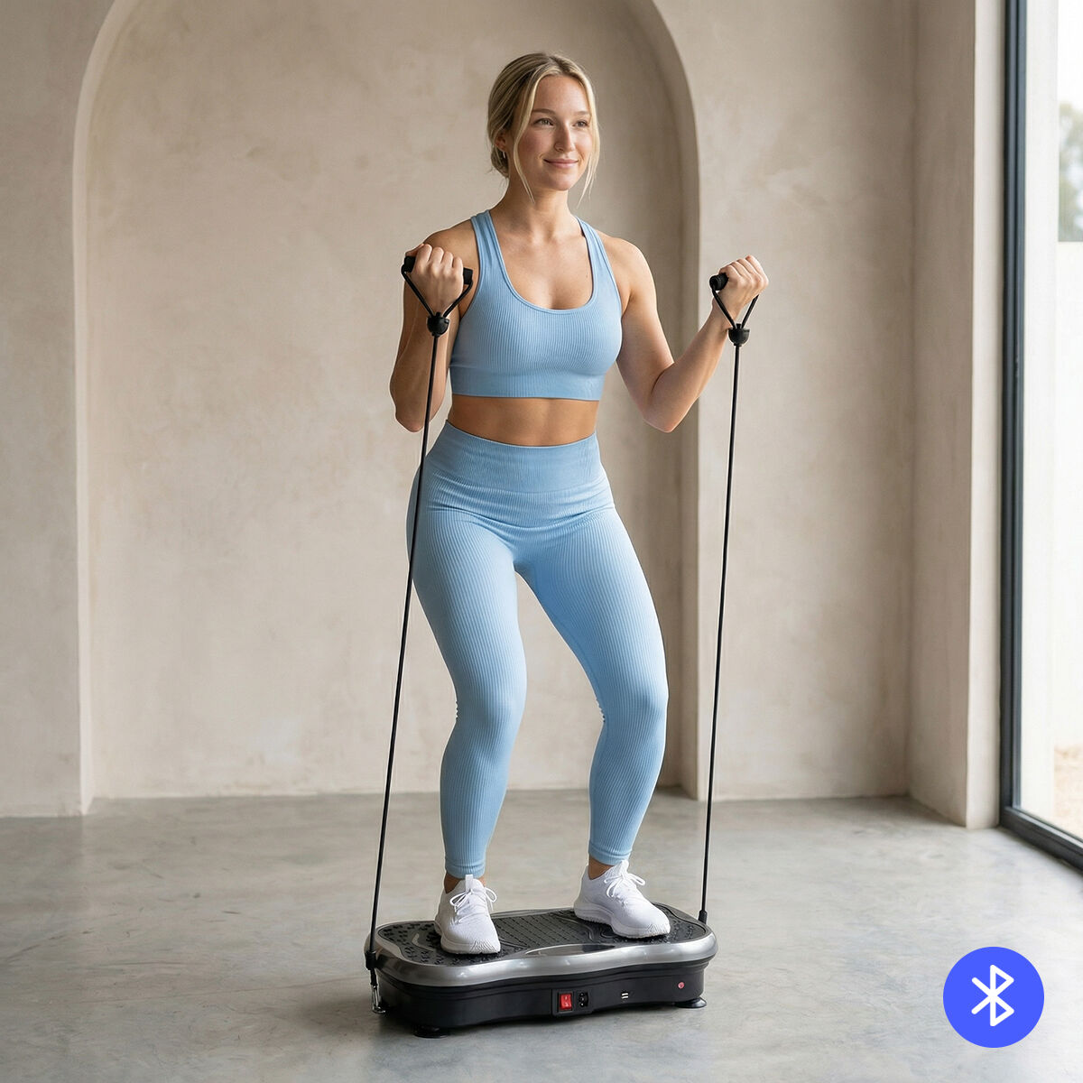 A woman in light blue workout attire stands on the vibration platform, using resistance bands. The background is a minimalist room with an arched wall.